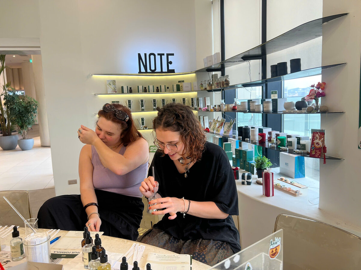 A traveler blending custom perfume at NOTE Lotte Mall West Lake Hanoi workshop - hands carefully measuring drops of essential oils
